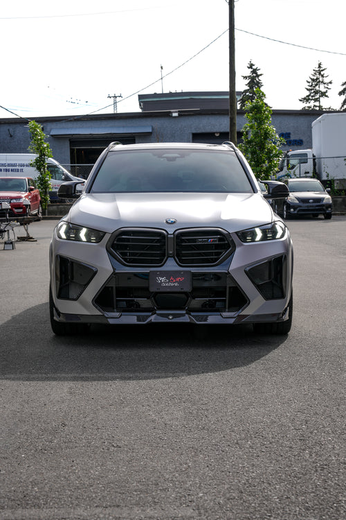 Gray BMW X5M featuring a REVOZPORT carbon fiber body kit with aggressive front lip, side skirts, and sporty aero styling parked outside a workshop.