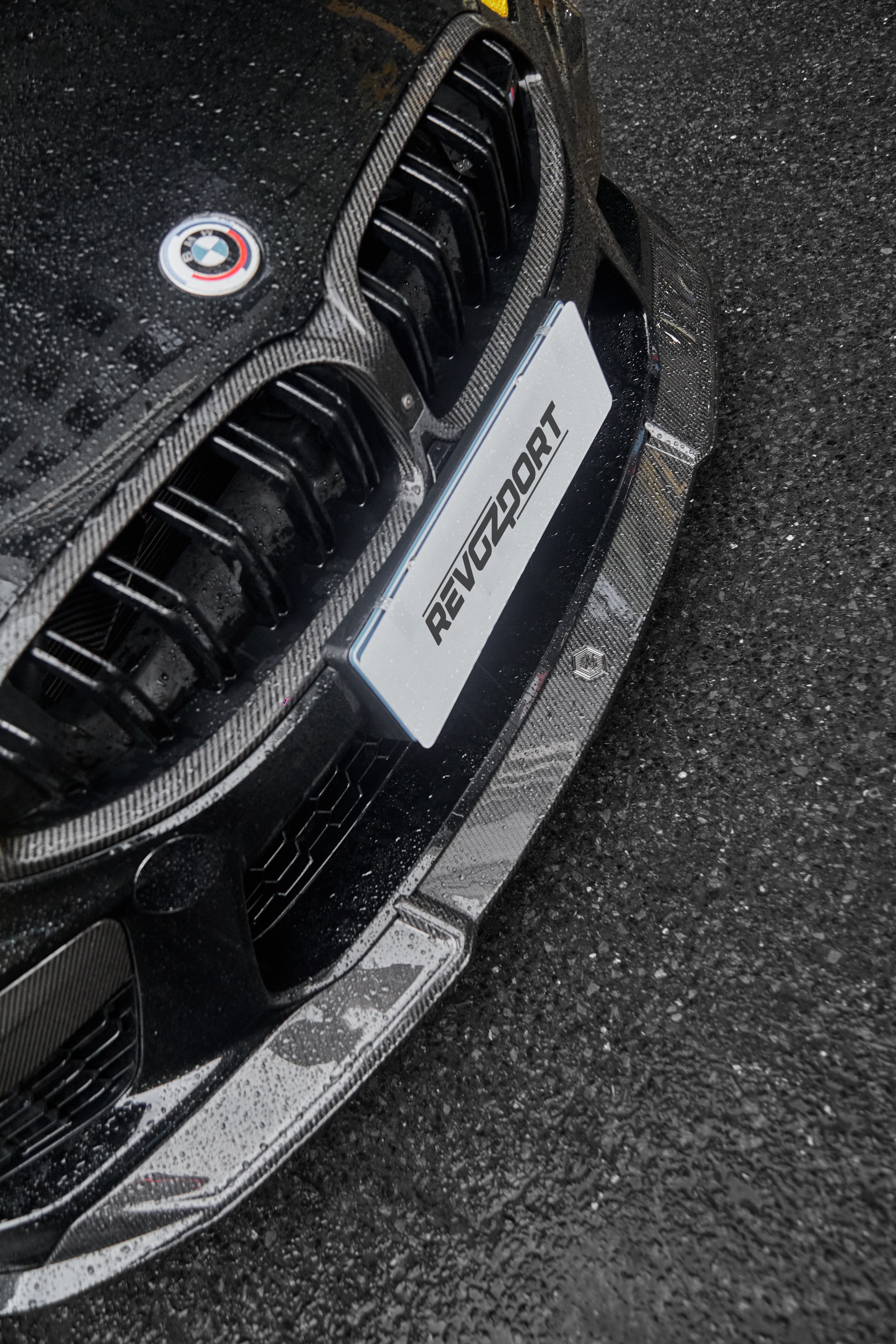 BMW with rain-covered carbon fiber front lip and grille, highlighting glossy weave texture and aggressive front aero styling.