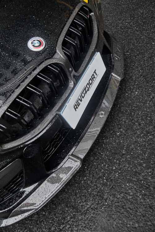 BMW with rain-covered carbon fiber front lip and grille, highlighting glossy weave texture and aggressive front aero styling.