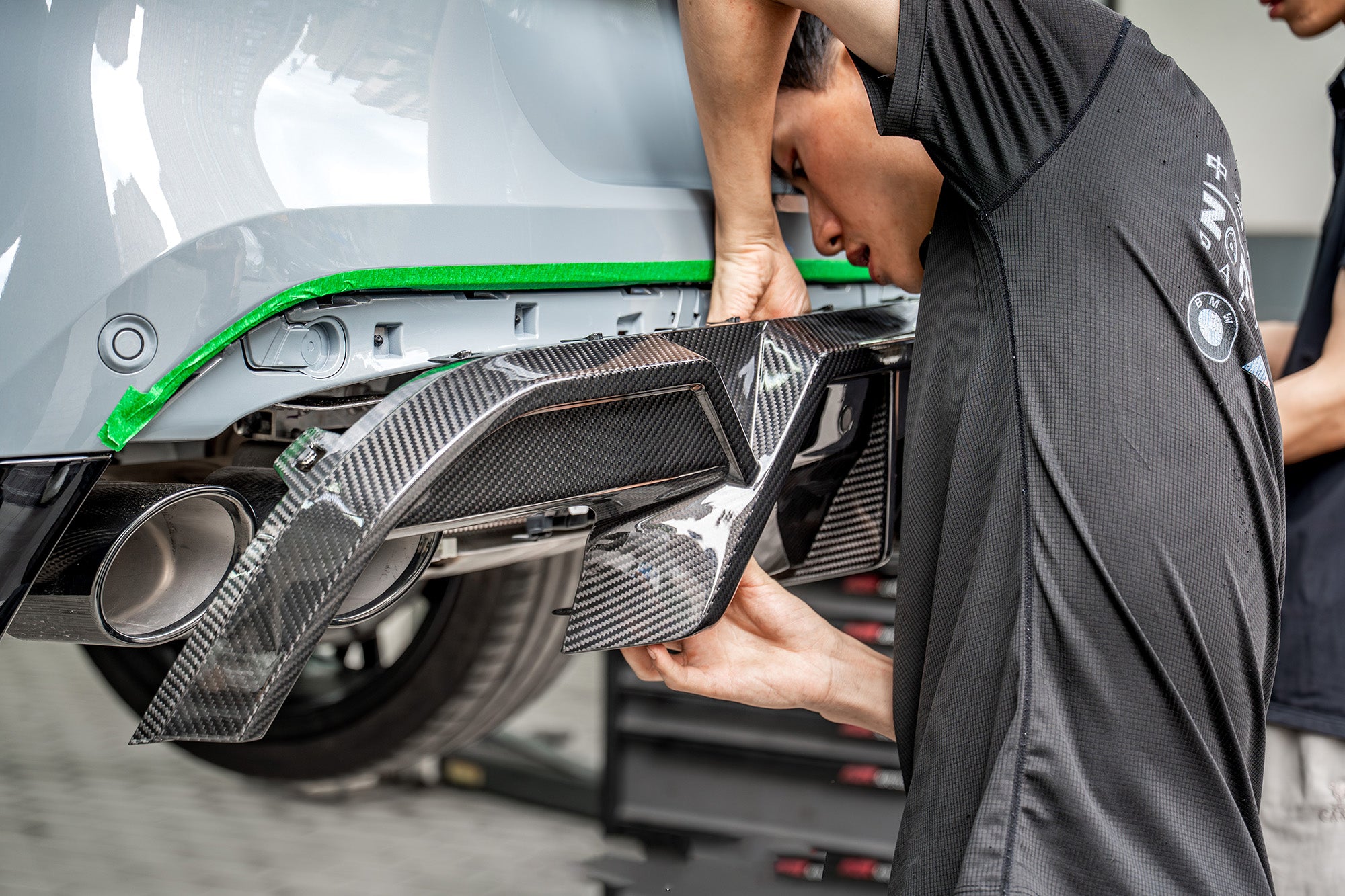 Hands-on carbon fiber diffuser installation highlighting precision fitment, detailed craftsmanship, and motorsport-inspired aero components inside a professional workshop environment.