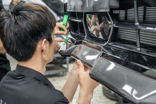Close-up installation scene of carbon fiber aero components, highlighting hands-on fitment work, precision craftsmanship, and performance-focused engineering details.