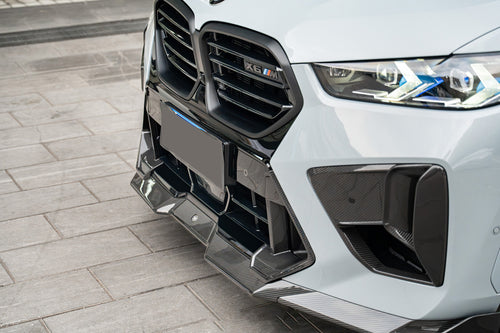 Detailed carbon fiber front aero close-up featuring aggressive splitter elements, precision vent design, and high-gloss composite surfaces under clean workshop lighting.