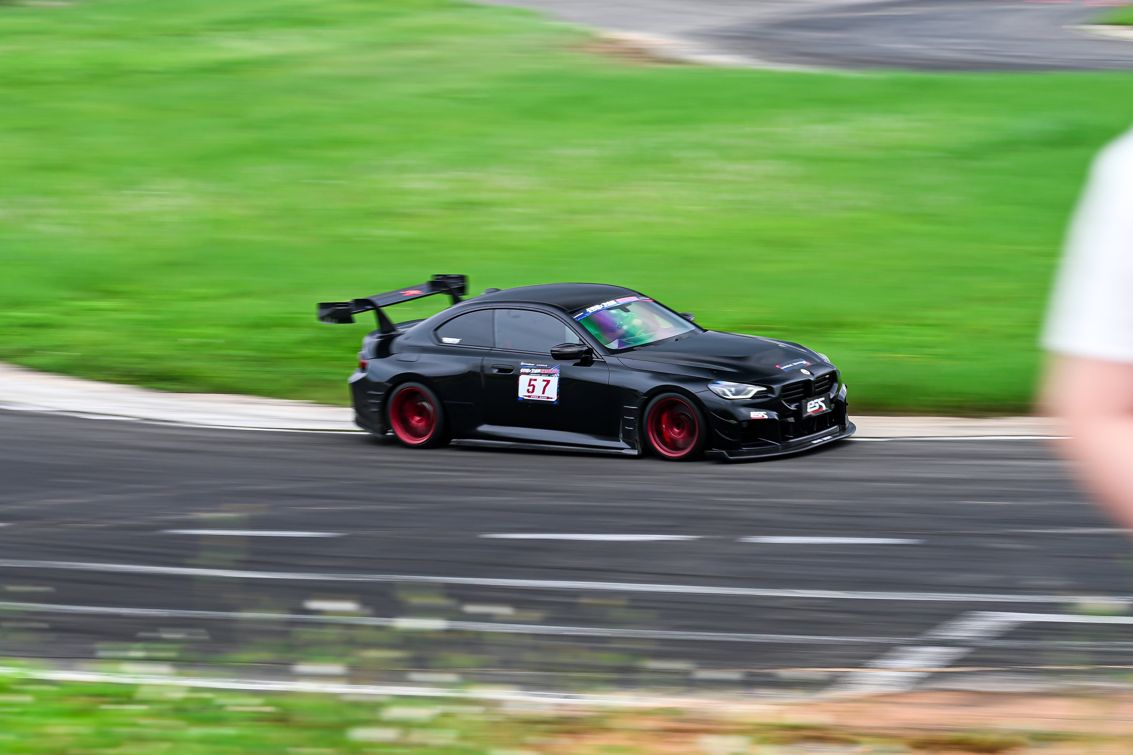Rolling shot of a black BMW on racetrack, featuring oversized rear wing, aggressive carbon fiber aero, lowered stance, and motorsport wheel setup.