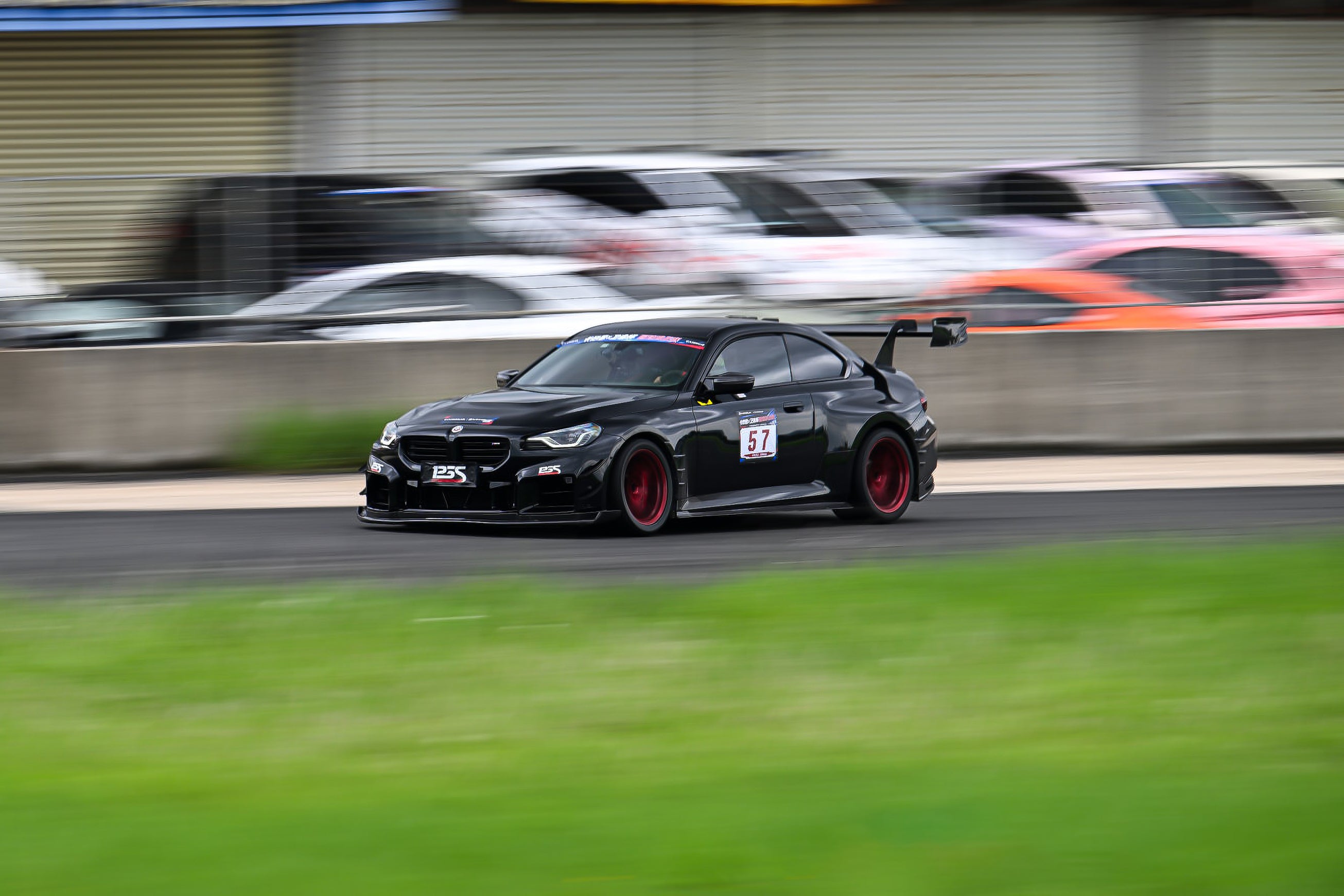 Rolling shot of a black BMW on racetrack, featuring oversized rear wing, aggressive carbon fiber aero, lowered stance, and motorsport wheel setup.