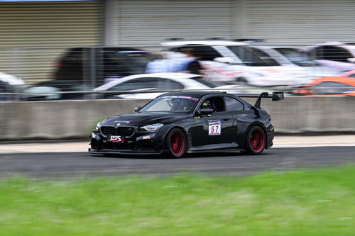 Rolling shot of a black BMW on racetrack, featuring oversized rear wing, aggressive carbon fiber aero, lowered stance, and motorsport wheel setup.