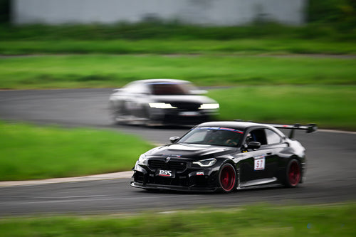 Rolling shot of a black BMW on racetrack, featuring oversized rear wing, aggressive carbon fiber aero, lowered stance, and motorsport wheel setup.