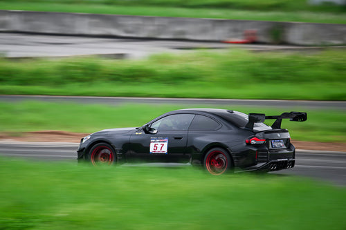Rolling shot of a black BMW on racetrack, featuring oversized rear wing, aggressive carbon fiber aero, lowered stance, and motorsport wheel setup.