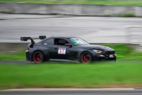 Rolling shot of a black BMW on racetrack, featuring oversized rear wing, aggressive carbon fiber aero, lowered stance, and motorsport wheel setup.
