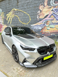 Silver BMW with carbon fiber body kit parked beside a colorful graffiti wall, highlighting front lip, hood vents, and aggressive styling.