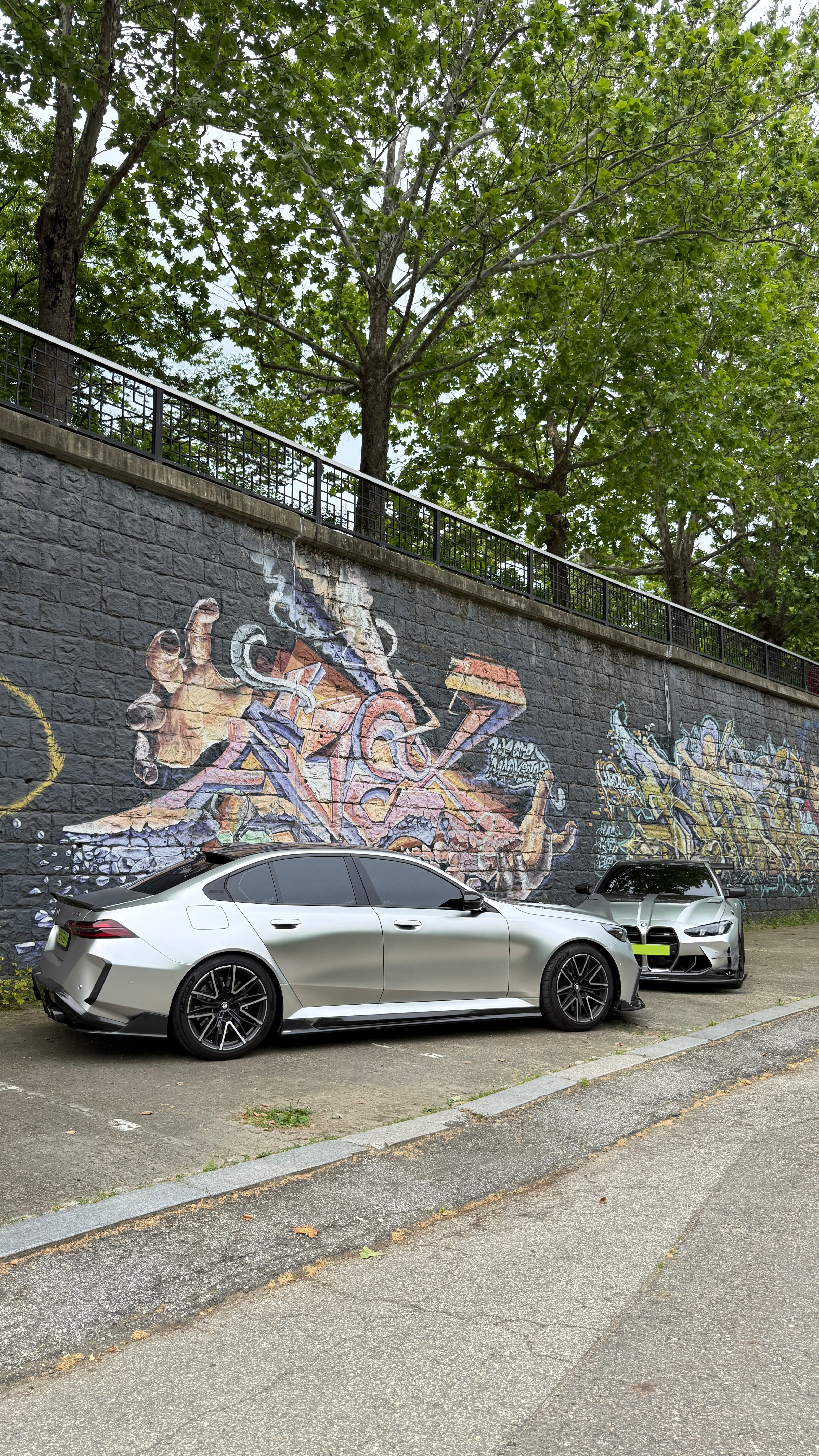 Top-down view of two BMWs with carbon fiber aero kits, hood vents, and rear wing parked beside a quiet road.