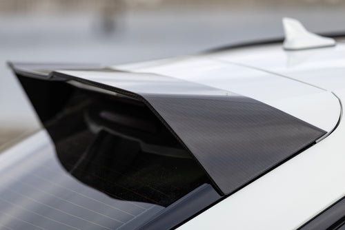White Audi RS6 Avant featuring a REVOZPORT carbon fiber body kit with front lip, side skirts, rear diffuser, and lowered stance parked in a modern urban waterfront setting.