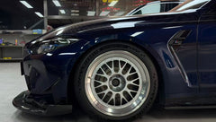 Dark blue BMW G82 M4 equipped with carbon fiber front splitter, side skirts, vented fenders, and a large rear wing, parked inside a modern luxury garage.