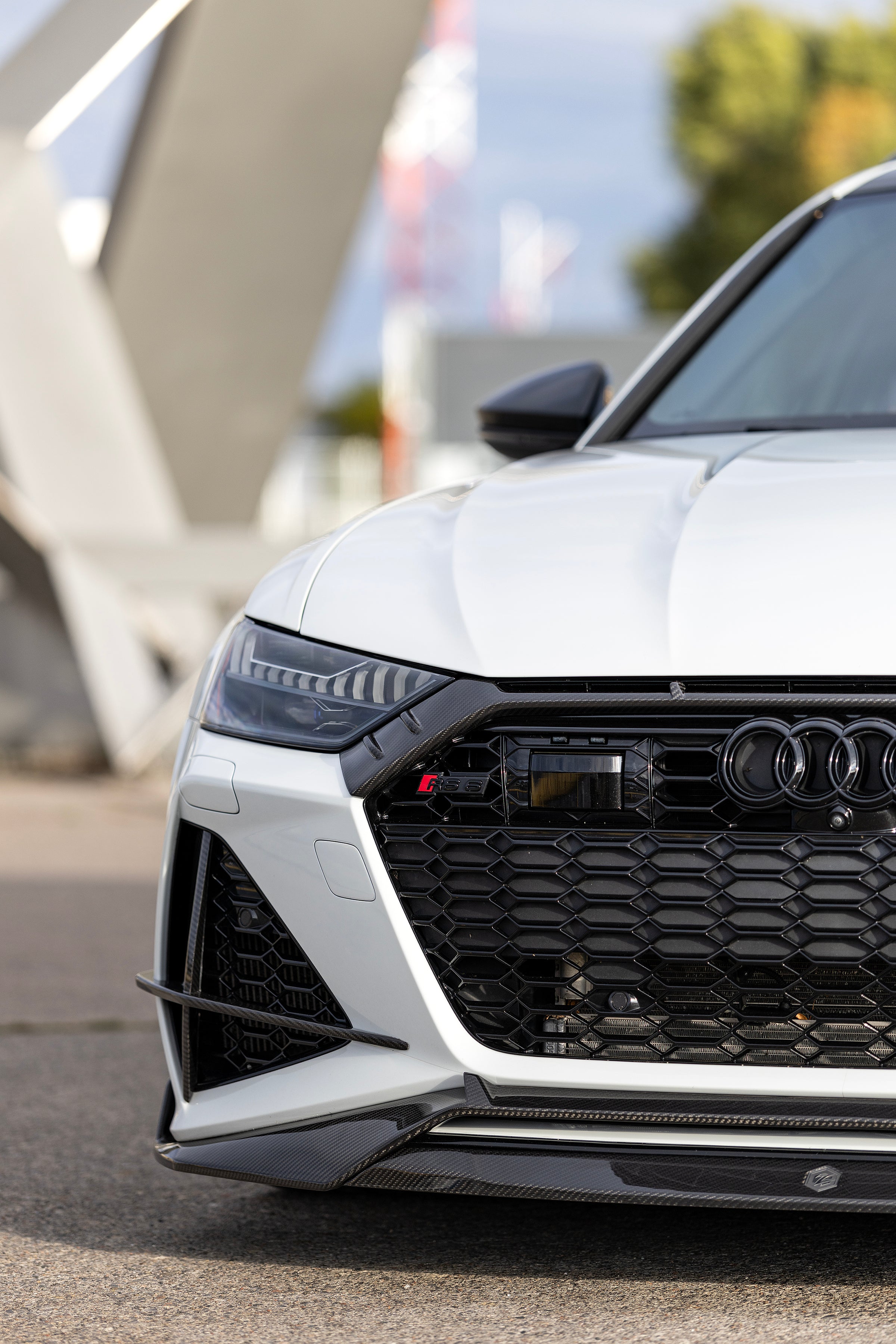 White Audi RS6 Avant featuring a REVOZPORT carbon fiber body kit with front lip, side skirts, and aggressive aero styling parked in front of a historic stone mansion during autumn.
