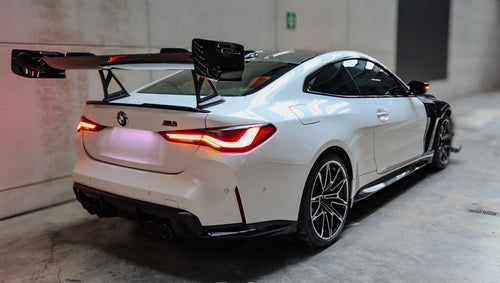 White BMW G82 M4 featuring a forged carbon fiber hood, front splitter, side canards, and aggressive aero styling parked inside a modern underground garage.