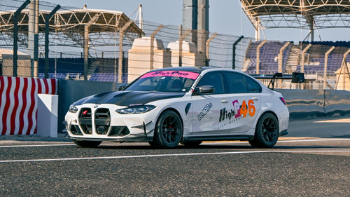 White BMW G80 M3 track car with REVOZPORT carbon fiber aero kit, front canards, rear wing, and racing decals driving on a professional race circuit.