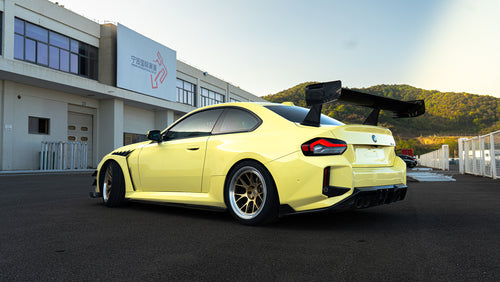 Rear three-quarter view of a BMW featuring oversized carbon fiber rear wing, aggressive widebody styling, bronze forged wheels, and track-focused aero details.