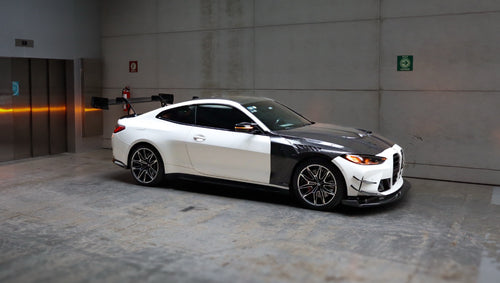 White BMW G82 M4 featuring a forged carbon fiber hood, front splitter, side canards, and aggressive aero styling parked inside a modern underground garage.
