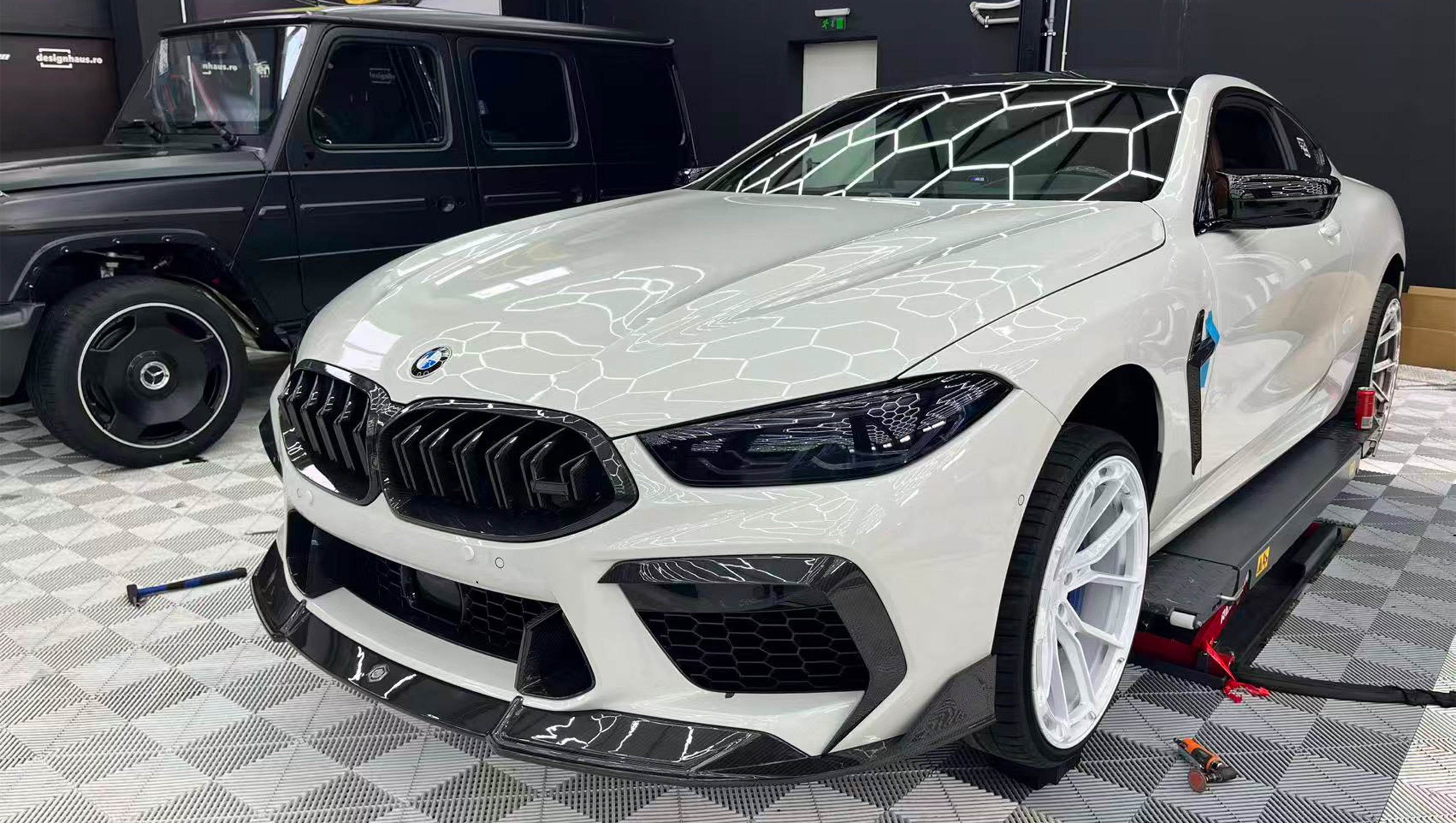White BMW F92 M8 featuring a REVOZPORT carbon fiber front lip, side skirts, black front grille, and white multi-spoke forged wheels parked at sunset on an open road.