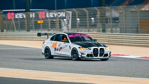 White BMW G80 M3 track car with REVOZPORT carbon fiber aero kit, front canards, rear wing, and racing decals driving on a professional race circuit.