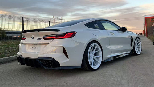 White BMW F92 M8 featuring a REVOZPORT carbon fiber front lip, side skirts, black front grille, and white multi-spoke forged wheels parked at sunset on an open road.
