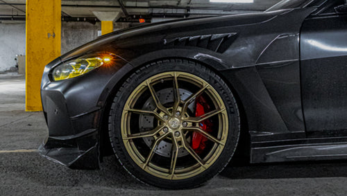 Close-up of a matte black BMW G82 M4 featuring REVOZPORT carbon fiber vented fenders, carbon side skirts, bronze forged wheels, and red performance brakes.
