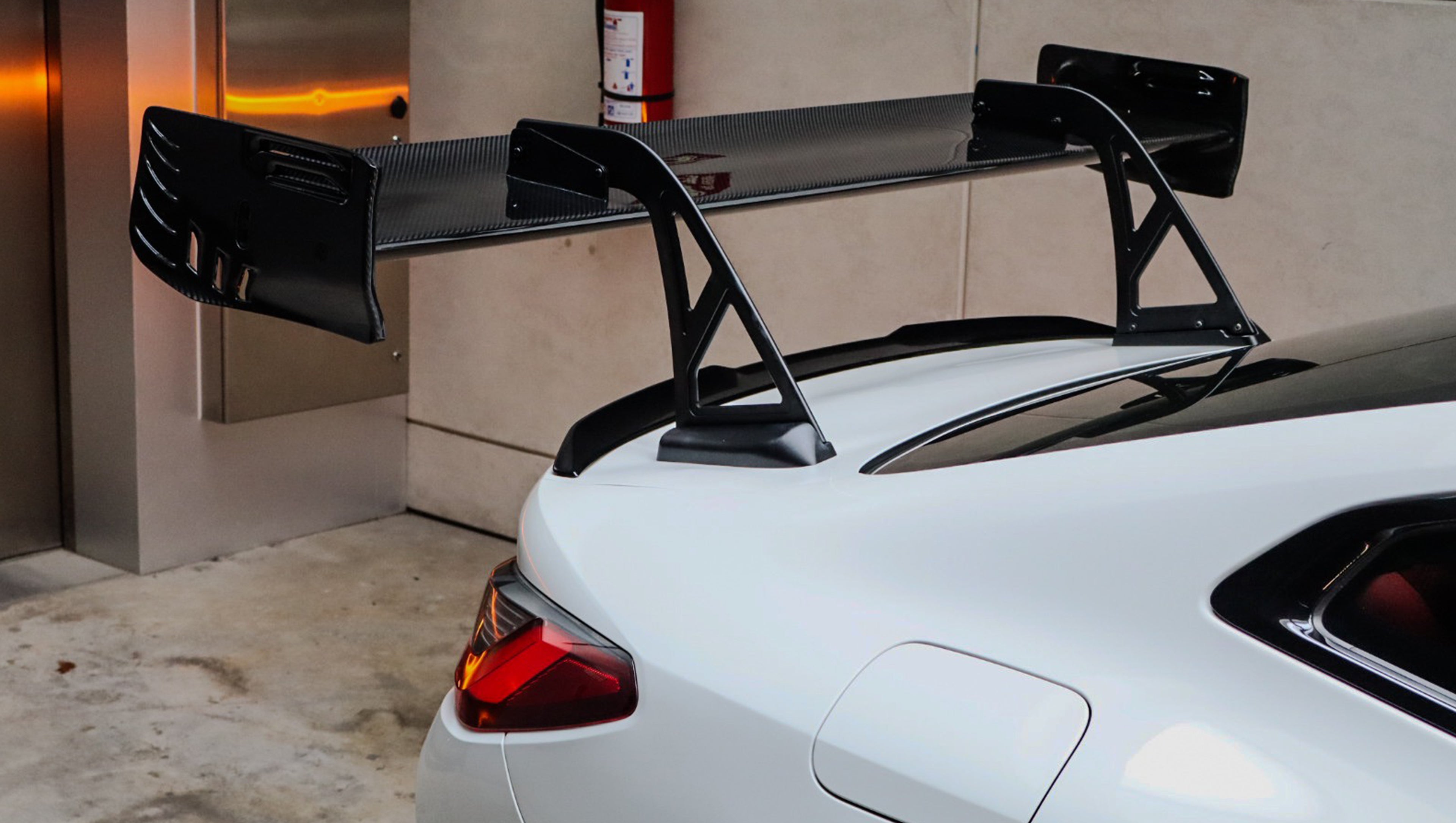 White BMW G82 M4 featuring a forged carbon fiber hood, front splitter, side canards, and aggressive aero styling parked inside a modern underground garage.