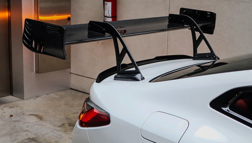 White BMW G82 M4 featuring a forged carbon fiber hood, front splitter, side canards, and aggressive aero styling parked inside a modern underground garage.