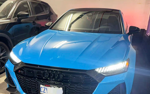 Blue Audi RS7 fitted with a REVOZPORT carbon fiber front lip and aggressive front aero styling, parked in an outdoor parking lot.