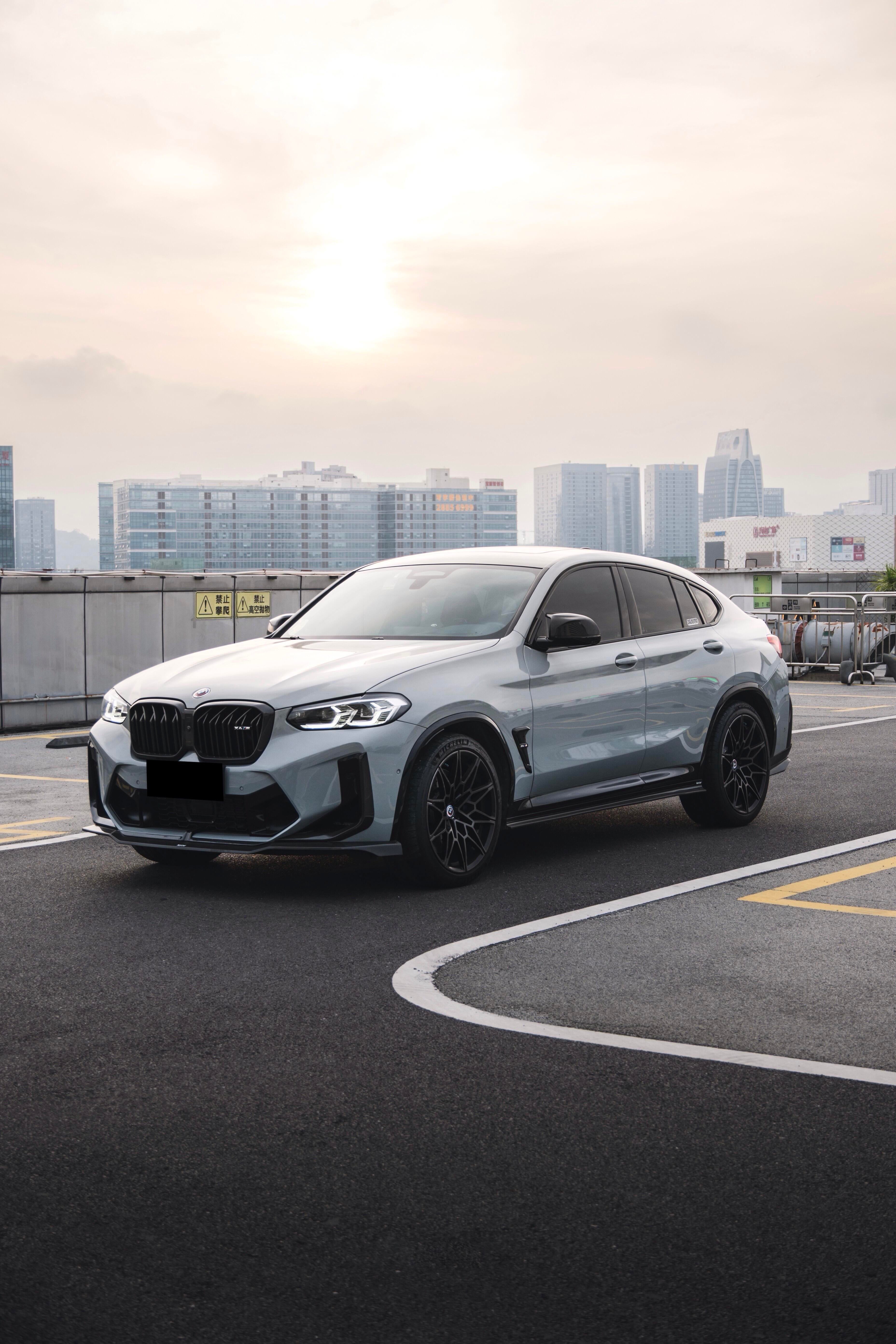 White BMW X4M featuring a REVOZPORT front grille upgrade and sporty front-end styling parked on an open urban road.