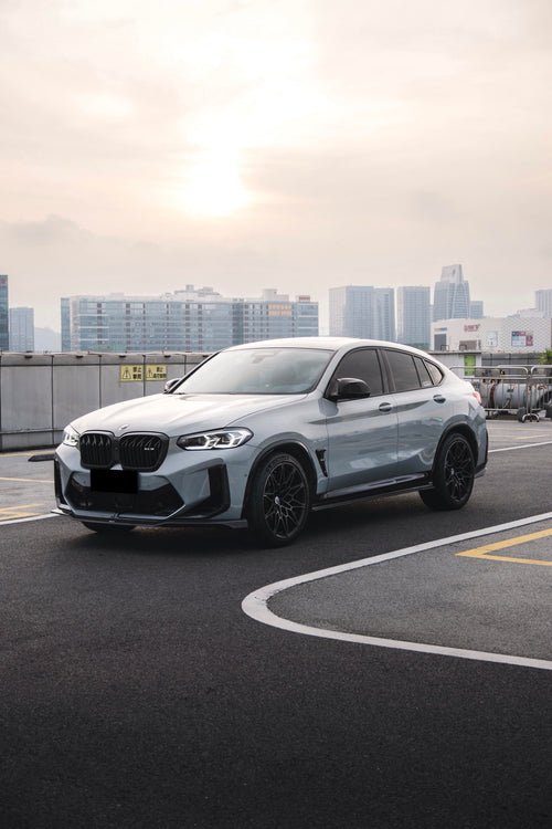 White BMW X4M featuring a REVOZPORT front grille upgrade and sporty front-end styling parked on an open urban road.