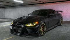 Side view of a matte black BMW G82 M4 featuring REVOZPORT carbon fiber side skirts, front lip, rear wing, and bronze forged wheels parked beside a brick wall.