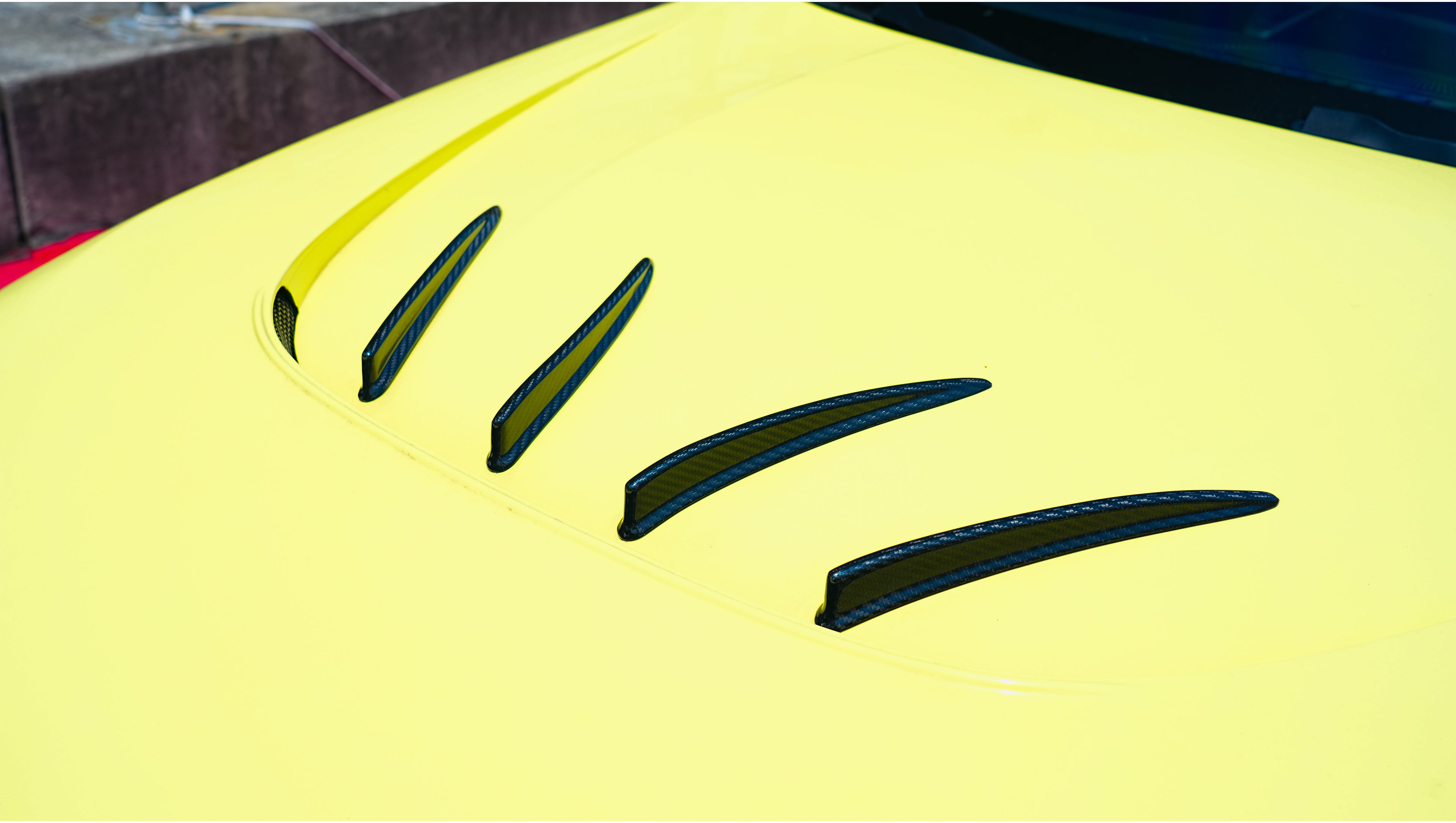 Yellow BMW G82 M4 with aggressive carbon fiber front splitter, vented hood, side canards, and bronze wheels parked on a race track pit lane.
