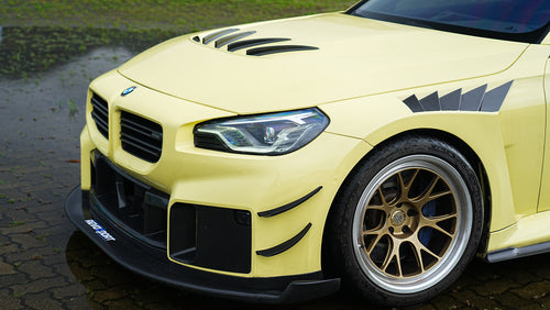 Close-up front quarter of a BMW featuring aggressive carbon fiber aero, vented hood, bronze forged wheels, and track-focused styling details.