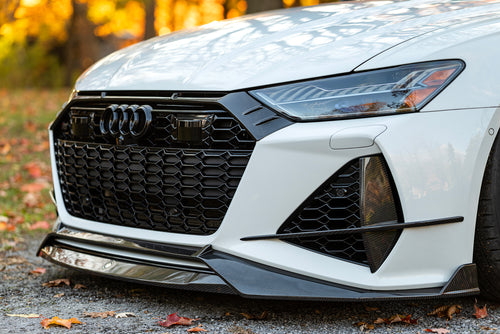 White Audi RS6 Avant featuring a REVOZPORT carbon fiber body kit with front lip, side skirts, and aggressive aero styling parked in front of a historic stone mansion during autumn.