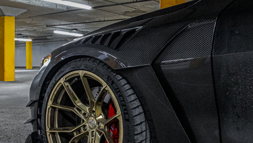 Close-up of a matte black BMW G82 M4 featuring REVOZPORT carbon fiber vented fenders, carbon side skirts, bronze forged wheels, and red performance brakes.