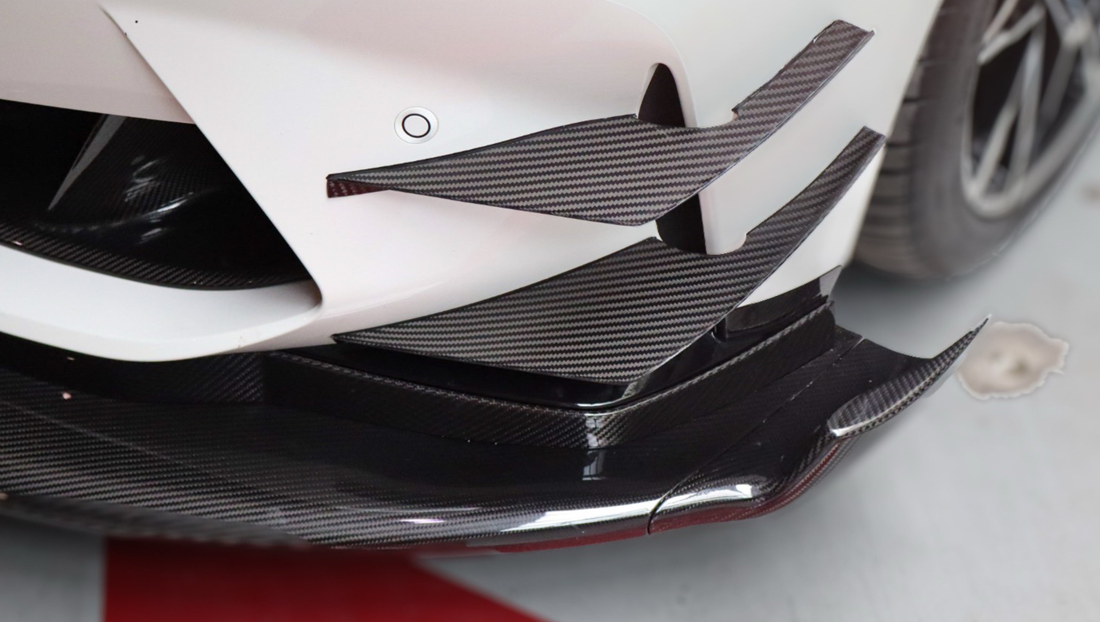White BMW G82 M4 featuring a forged carbon fiber hood, front splitter, side canards, and aggressive aero styling parked inside a modern underground garage.
