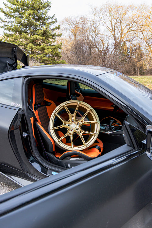 Interior detail of a BMW featuring bronze forged wheel fitment, carbon fiber cabin accents, and stripped track-focused atmosphere.