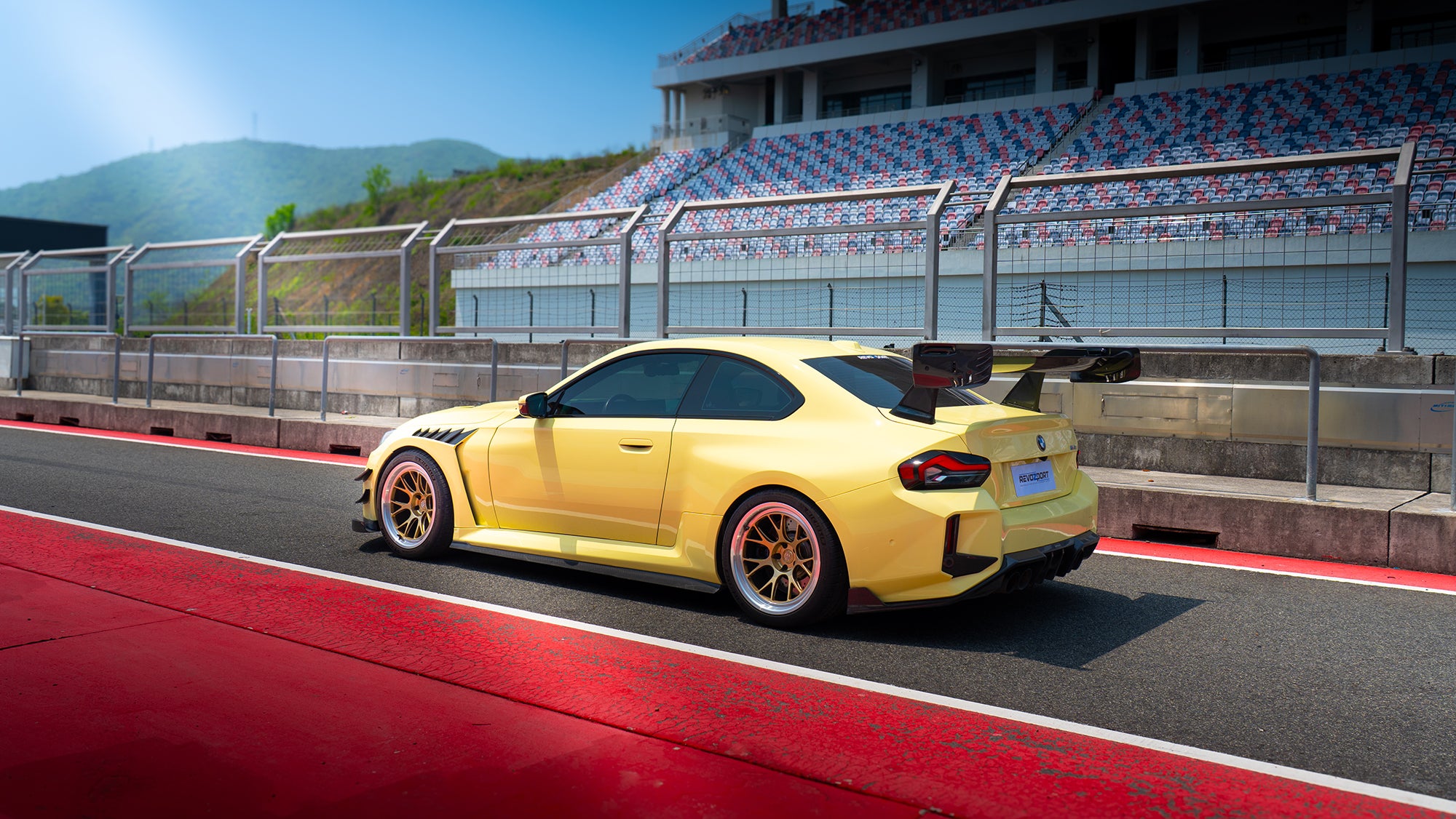 Rear three-quarter view of a BMW on racetrack pit lane, featuring carbon fiber widebody aero, oversized rear wing, and forged motorsport wheels.