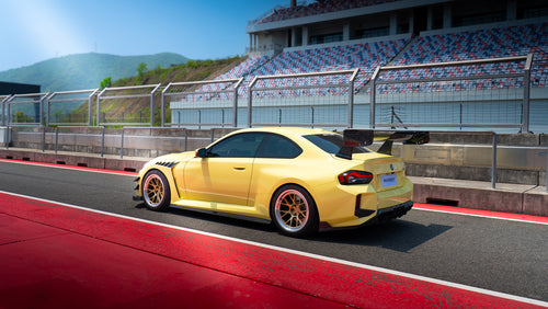 Rear three-quarter view of a BMW on racetrack pit lane, featuring carbon fiber widebody aero, oversized rear wing, and forged motorsport wheels.
