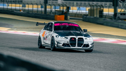 White BMW G80 M3 track car with REVOZPORT carbon fiber aero kit, front canards, rear wing, and racing decals driving on a professional race circuit.
