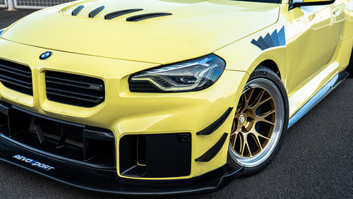 Close-up detail of a BMW front end featuring aggressive carbon fiber aero, vented hood, forged bronze wheels, and track-inspired styling.