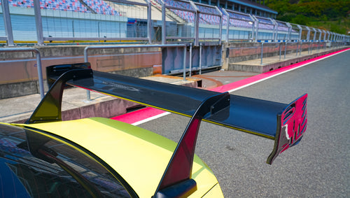 Yellow BMW G82 M4 with aggressive carbon fiber front splitter, vented hood, side canards, and bronze wheels parked on a race track pit lane.