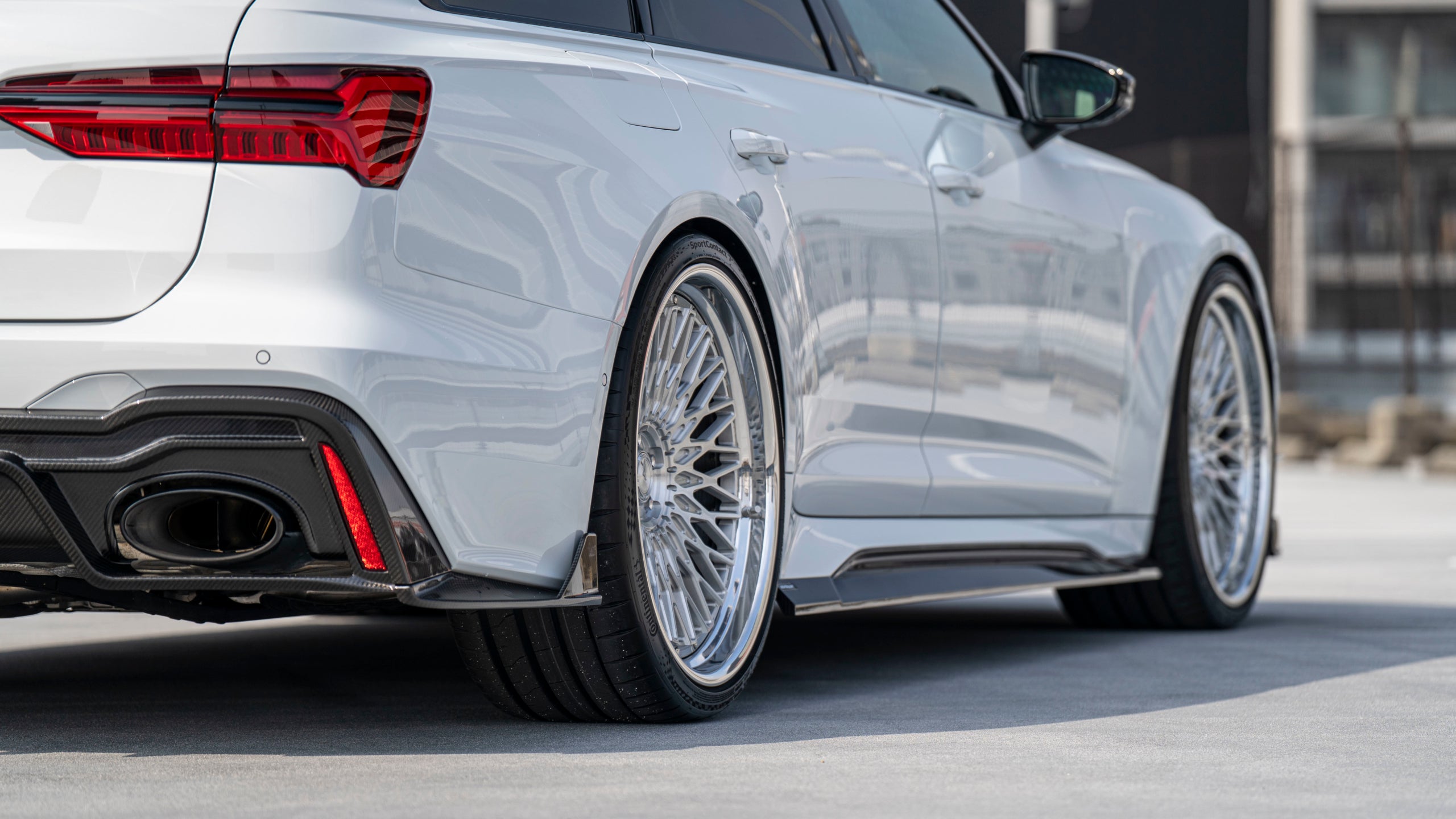 White Audi RS6 Avant featuring a REVOZPORT carbon fiber body kit with front lip, side skirts, rear diffuser, and lowered stance driving at high speed on a highway.