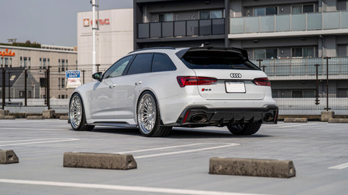White Audi RS6 Avant featuring a REVOZPORT carbon fiber body kit with front lip, side skirts, rear diffuser, and lowered stance driving at high speed on a highway.