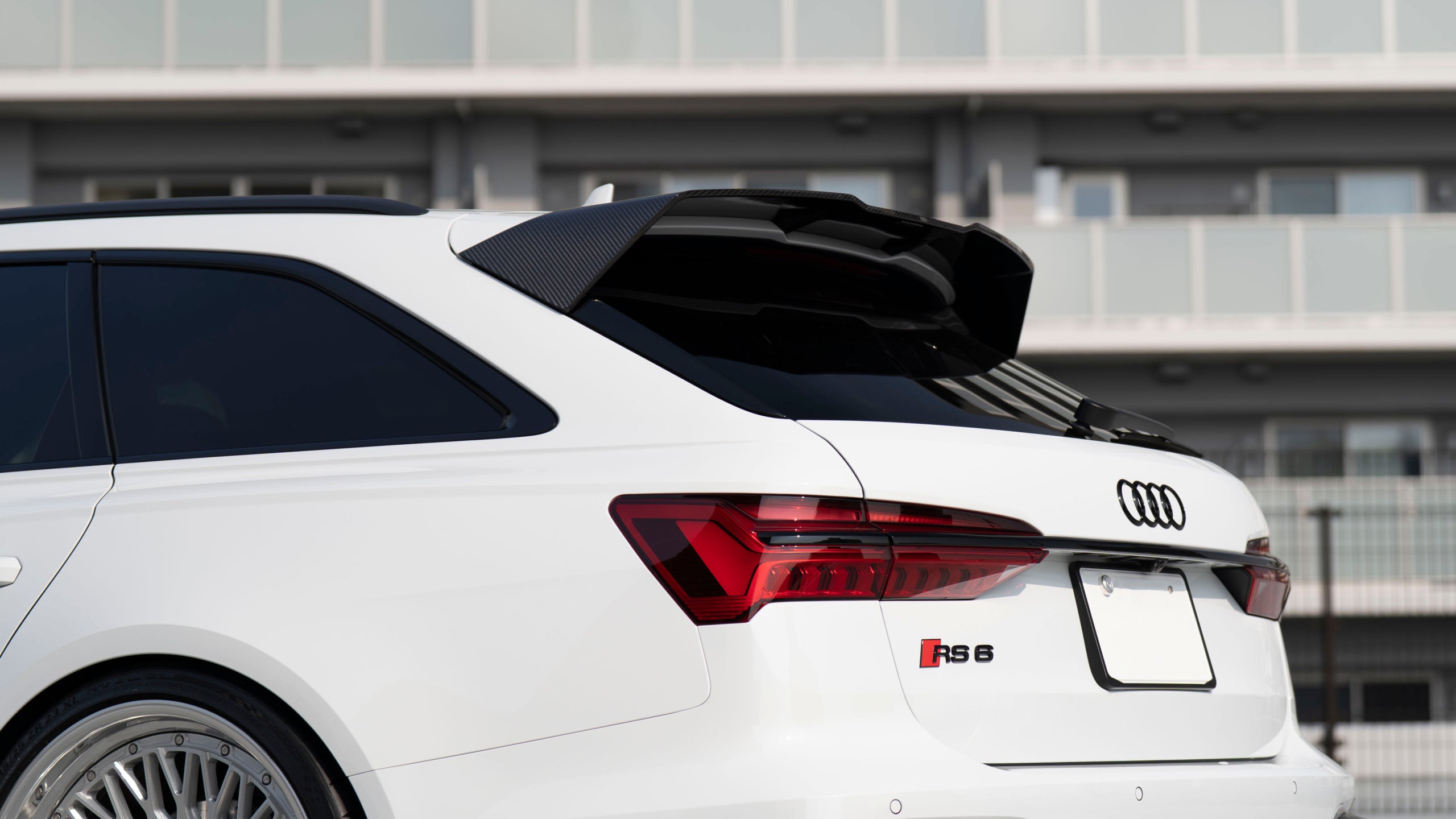 White Audi RS6 Avant featuring a REVOZPORT carbon fiber body kit with front lip, side skirts, rear diffuser, and lowered stance driving at high speed on a highway.