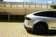Silver Tesla Model X featuring a REVOZPORT body kit with carbon fiber front lip, side skirts, wide fender flares, and lowered stance parked outdoors in sunlight.