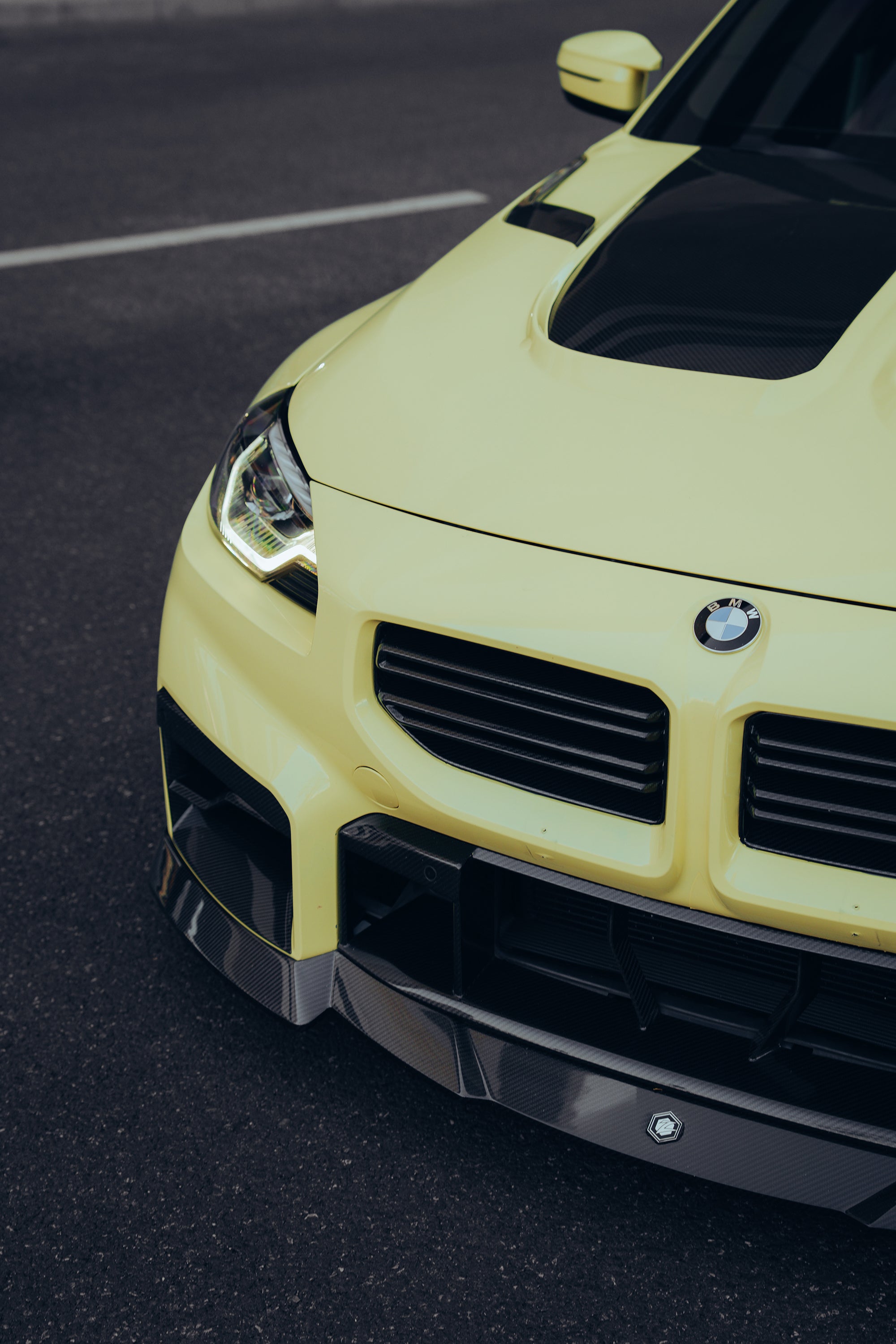 Close-up of a yellow BMW with carbon fiber front lip and hood vents, highlighting aggressive front aero styling.