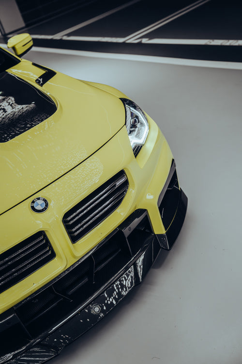 Close-up of the front of the BMW M2, featuring a carbon fiber surround, photographed in a high-end studio with lights on, equipped with a front grille, front lip, and engine cover