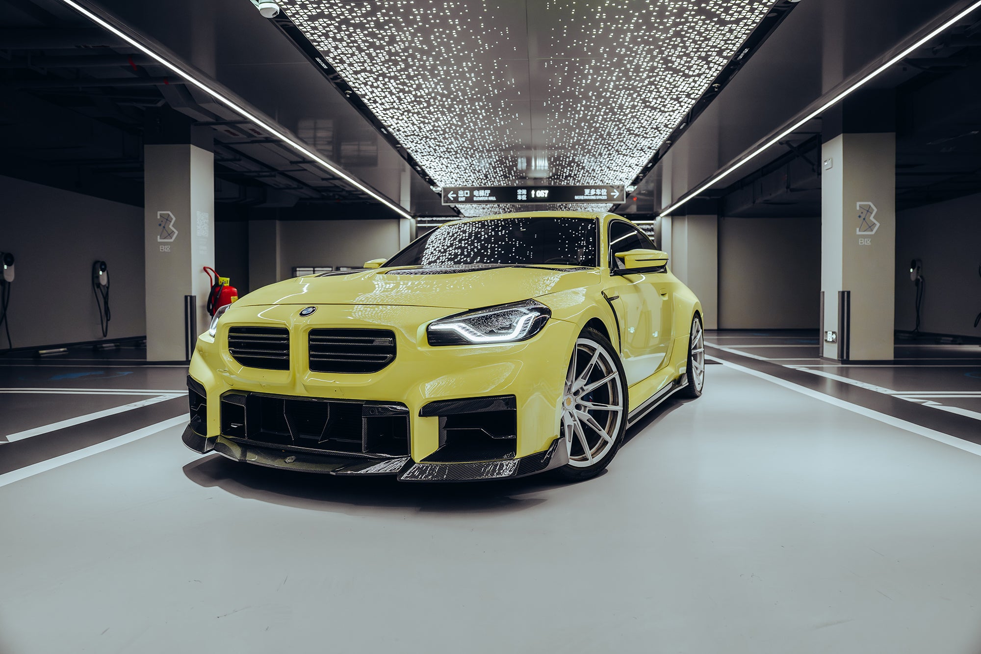 Yellow BMW with carbon fiber body kit parked in a modern garage, highlighting its aggressive front styling and performance-inspired design.