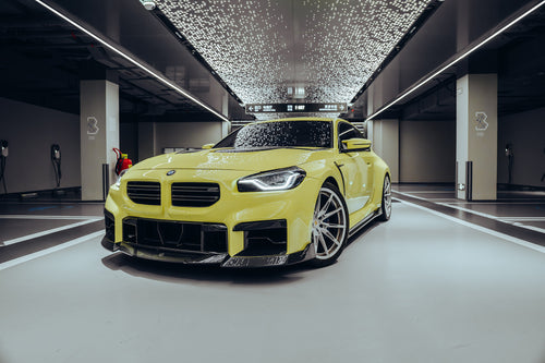 Yellow BMW with carbon fiber body kit parked in a modern garage, highlighting its aggressive front styling and performance-inspired design.